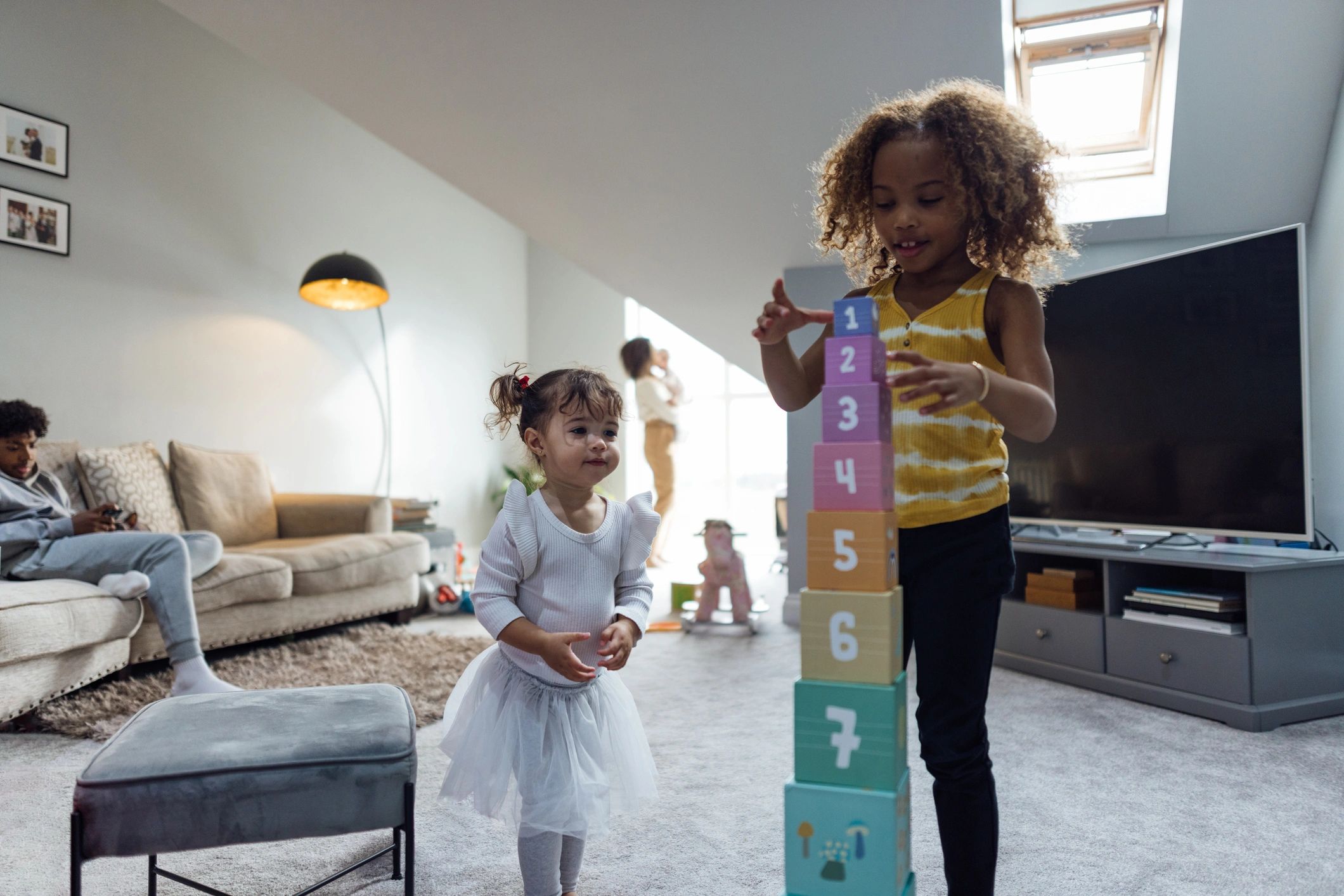 Young girl building a tower of toy blocks while family watches