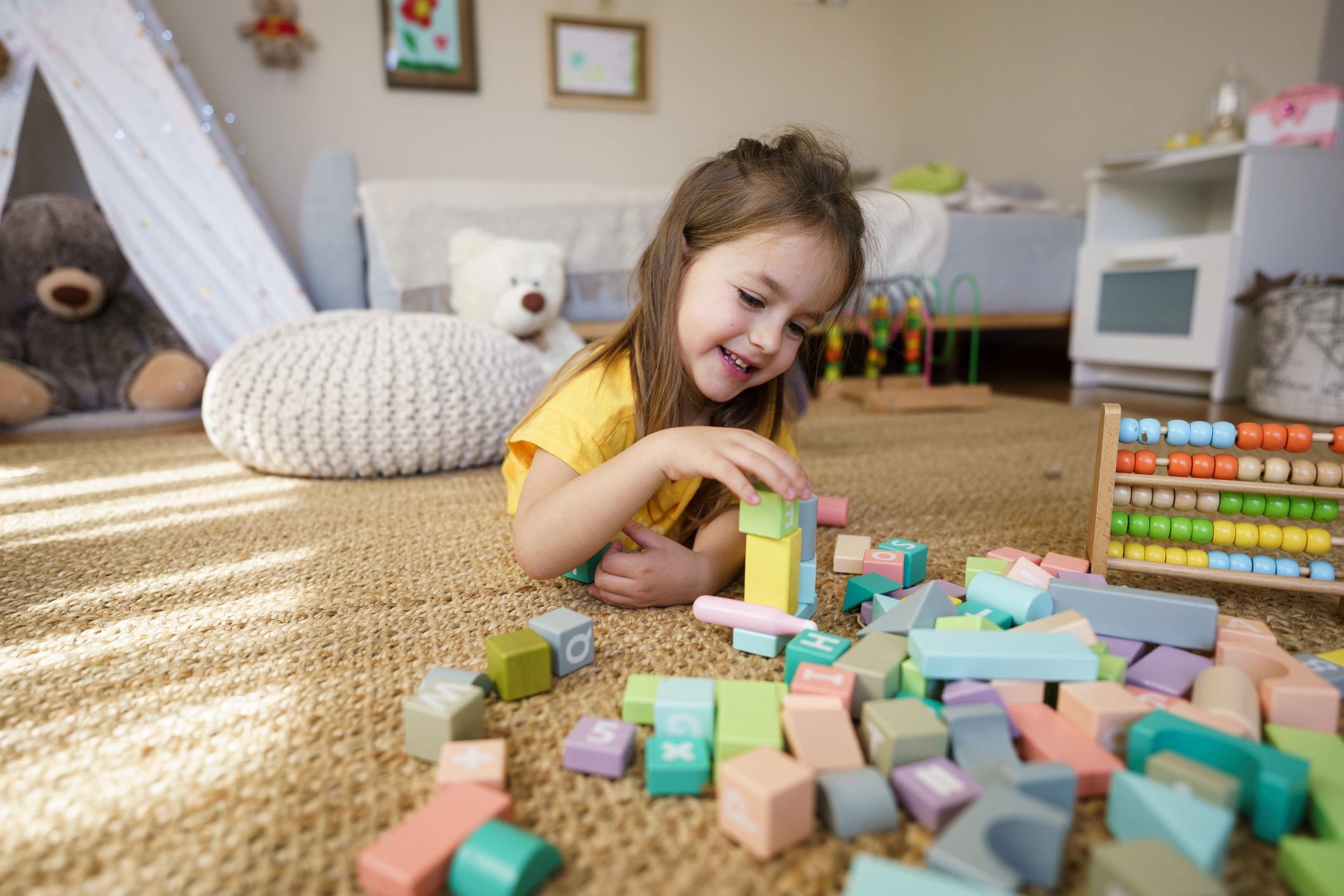 Happy little girl playing with colourful wooden blocks on the floor